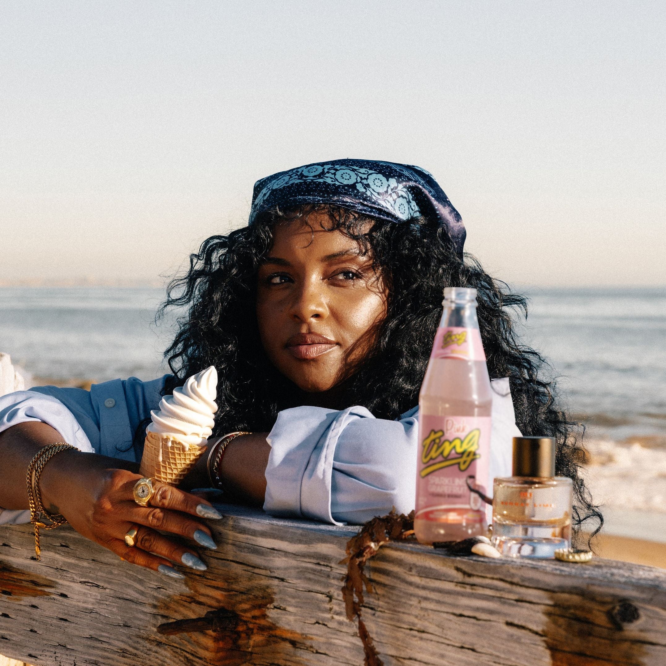 Woman on a beach with ice cream, a bottle, and a bag of chips.